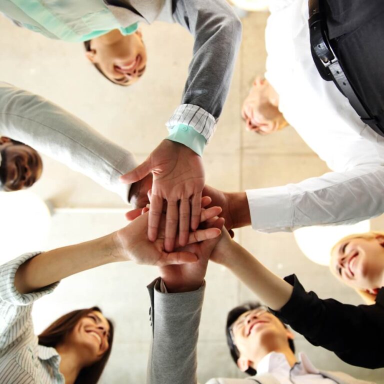 Diverse business team standing together with hands joined, representing collaboration, trust, and shared purpose.
